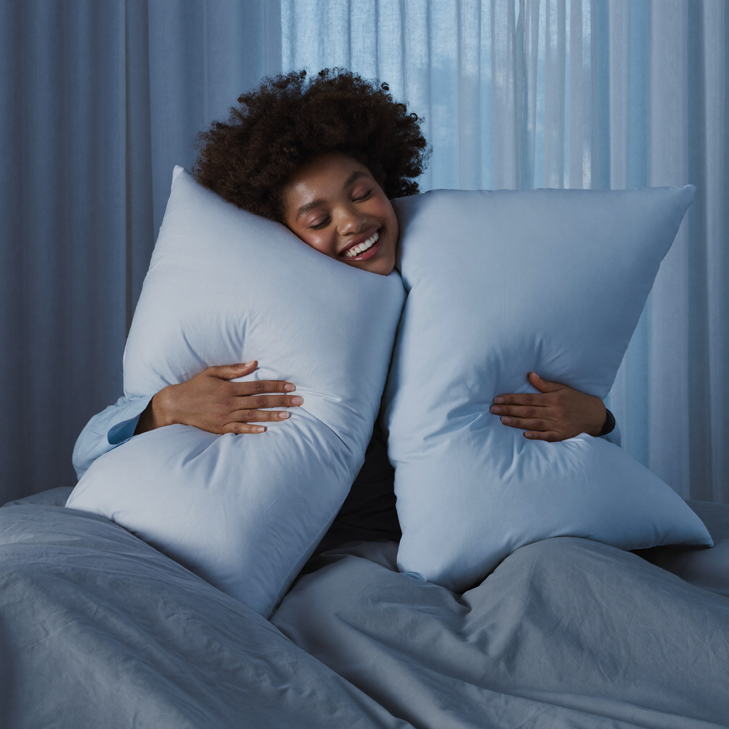 Happy woman hugging plush cool-blue Frostmoor cooling pillows in a serene bedroom