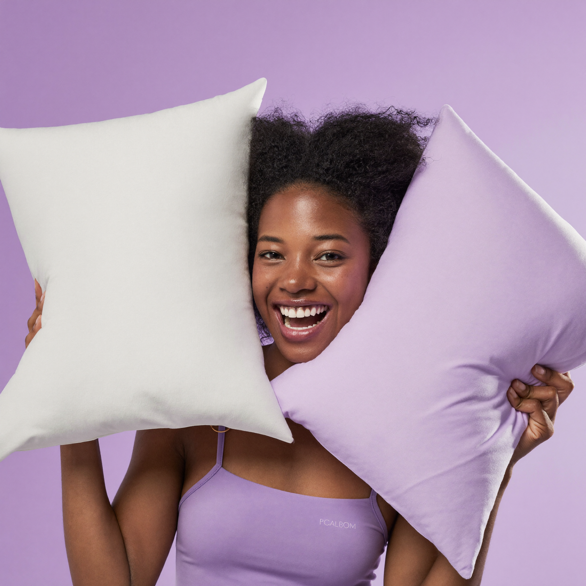 Joyful woman presenting white and lavender Frostmoor cooling pillowcases on a soft lavender studio background