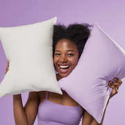 Joyful woman presenting white and lavender Frostmoor cooling pillowcases on a soft lavender studio background