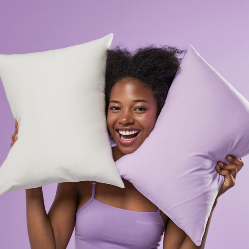 Joyful woman presenting white and lavender Frostmoor cooling pillowcases on a soft lavender studio background